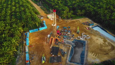imágenes cinematográficas de drones de 4k de la estructura del equipo de la plataforma de perforación en tierra para la exploración y explotación de petróleo en medio de la jungla rodeada de palmeras durante la puesta de sol y el alto precio del petróleo
