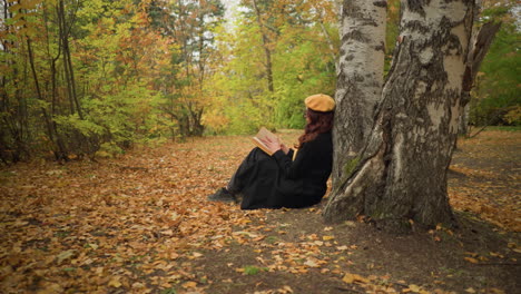 side view of lady flipping through book thoughtfully while leaning against tree, autumn leaves cover the ground as she enjoys peaceful solitude in serene nature, absorbed in pages of knowledge