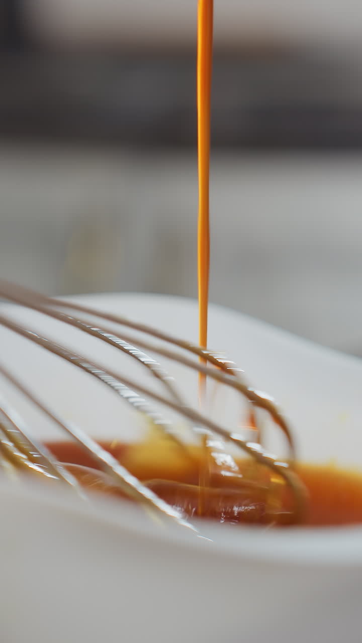 Primo piano di una persona che versa una zuppa rosso intenso in una ciotola bianca mentre mescola con una frusta. Il liquido vibrante scorre uniformemente mentre gli ingredienti si mescolano, creando una miscela saporita in una cucina moderna.