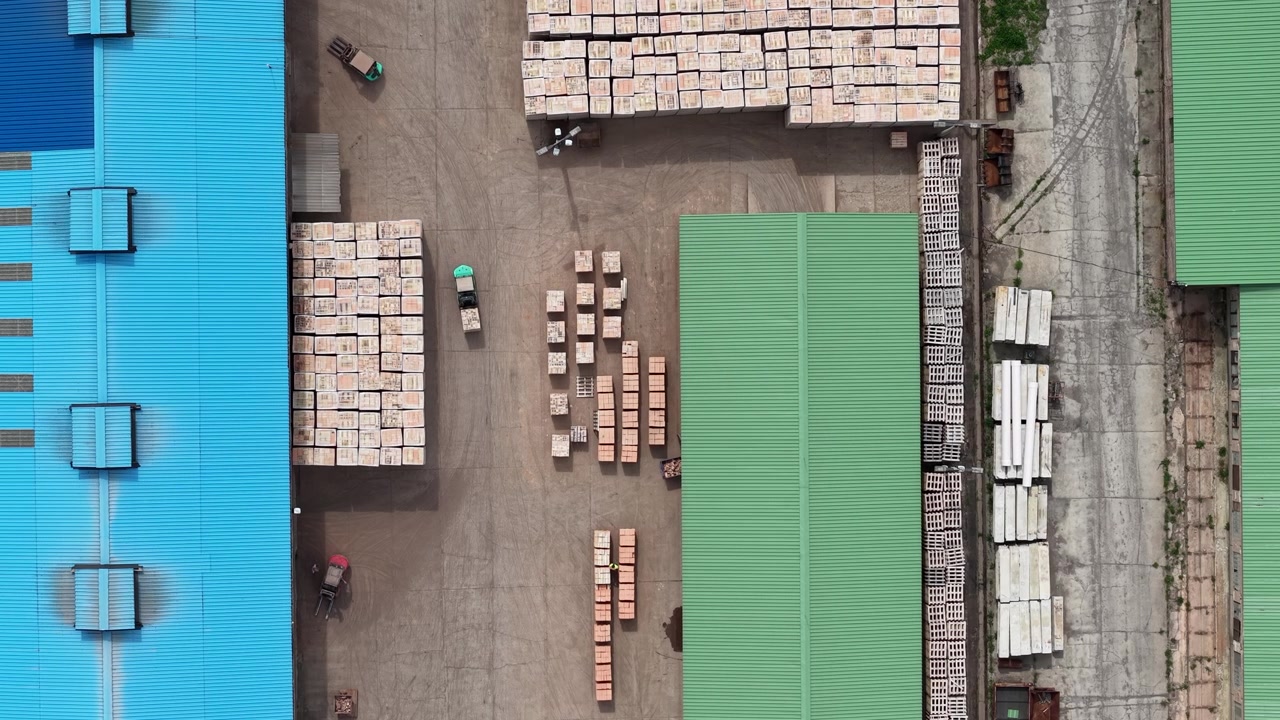 Una vista aerea cattura un vivace complesso industriale con una vasta gamma di materiali da costruzione e carrelli elevatori in attività, che simboleggia operazioni efficienti della catena di approvvigionamento.