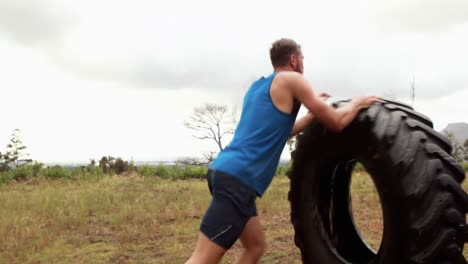 hombre en forma empujando un neumático pesado durante una carrera de obstáculos