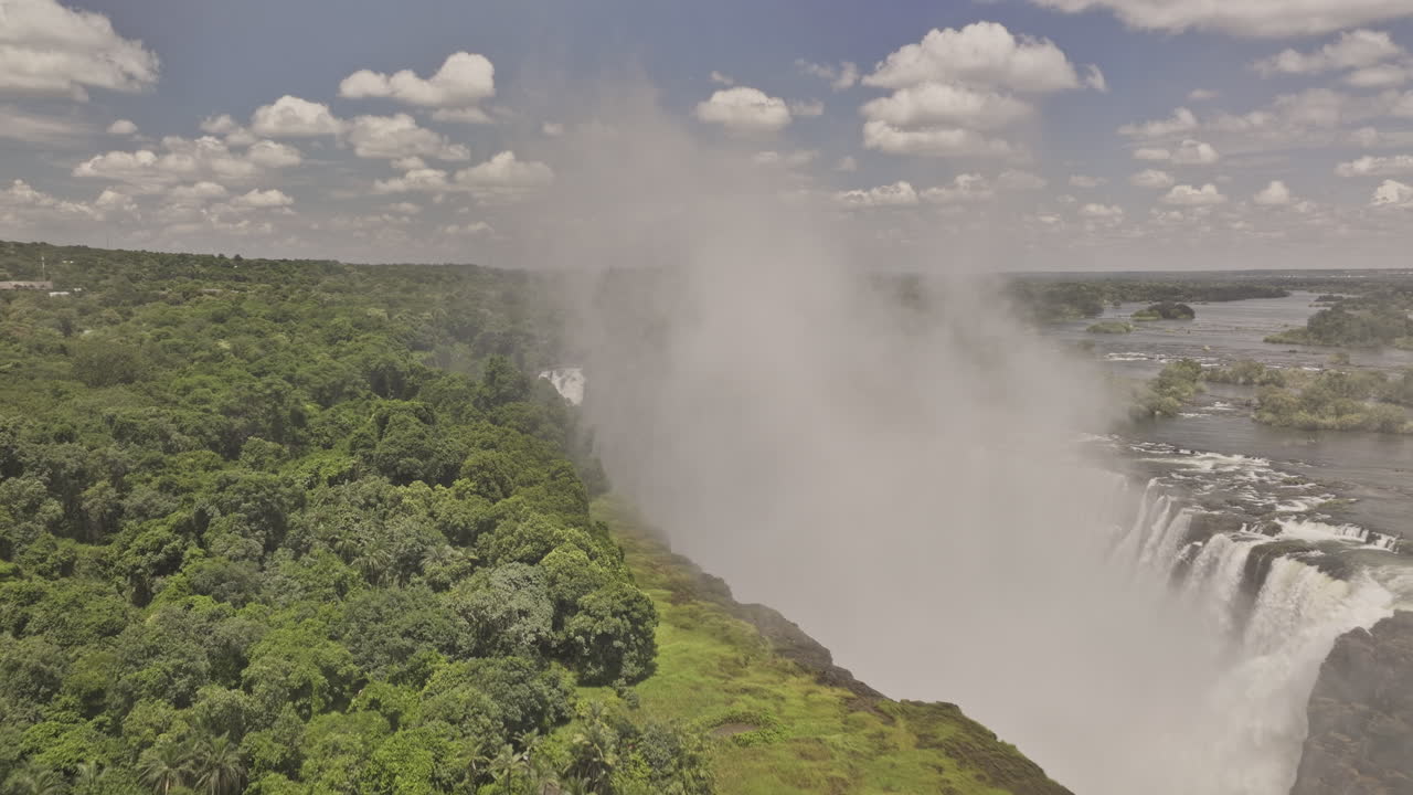 Victoria Falls Zimbabwe Aerial v17 flyover along cliffside capturing misty gorge, Zambezi River, a thunderous waterfall plunges into pool beneath rainbow - Shot with Mavic 3 Pro Cine - Jan 3rd 2024