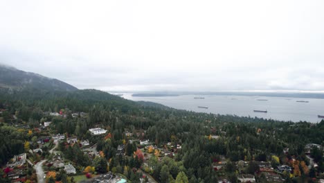 Barcos-De-Carga-Atracados-En-El-Océano-Junto-A-Un-Barrio-Montañoso,-A-Lo-Largo-De-La-Entrada-De-Vancouver-En-Otoño,-Día-Nublado