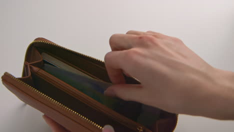 A caucasian woman&#039;s hands opening a brown wallet, pulling out a Canadian $20 bill and $10 bill, and placing them on the table