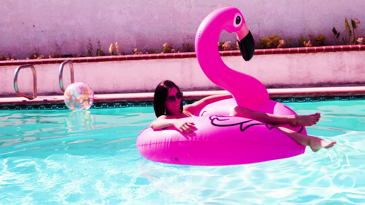 Female enjoying the sun, floating in the pool in a bathing suit