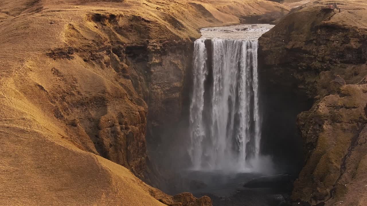 aerial - Skógafoss waterfall plunging into dark basin in south Iceland