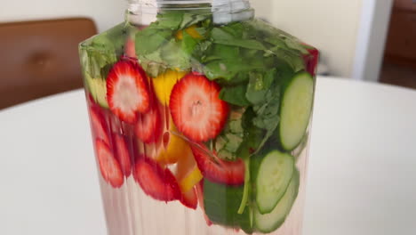 cerca de una jarra de vidrio llena de agua de spa con infusión de fruta, fresa de limón y albahaca