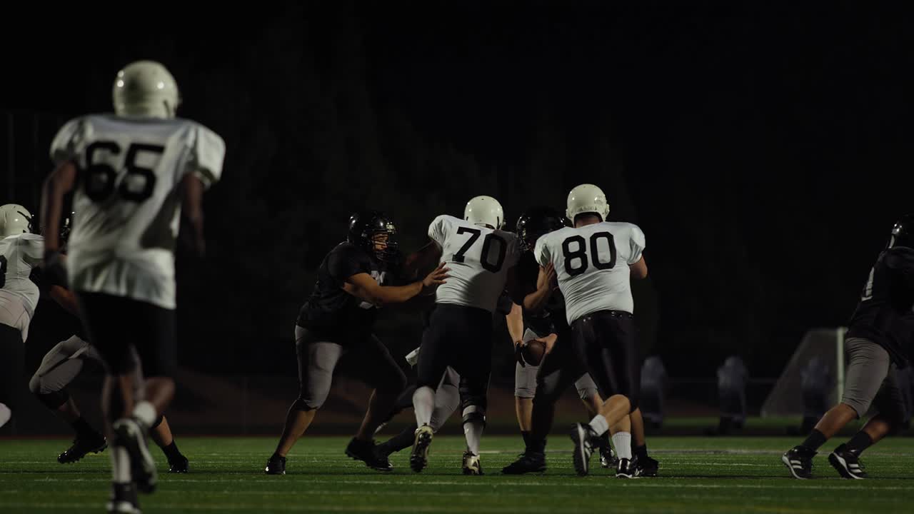 A football player fights his way down the field toward the end zone at night