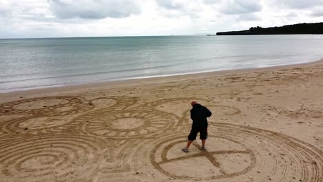 vista aérea hombre en órbita creando interesante zen diseño de arte de arena en la ventosa playa galesa dorada