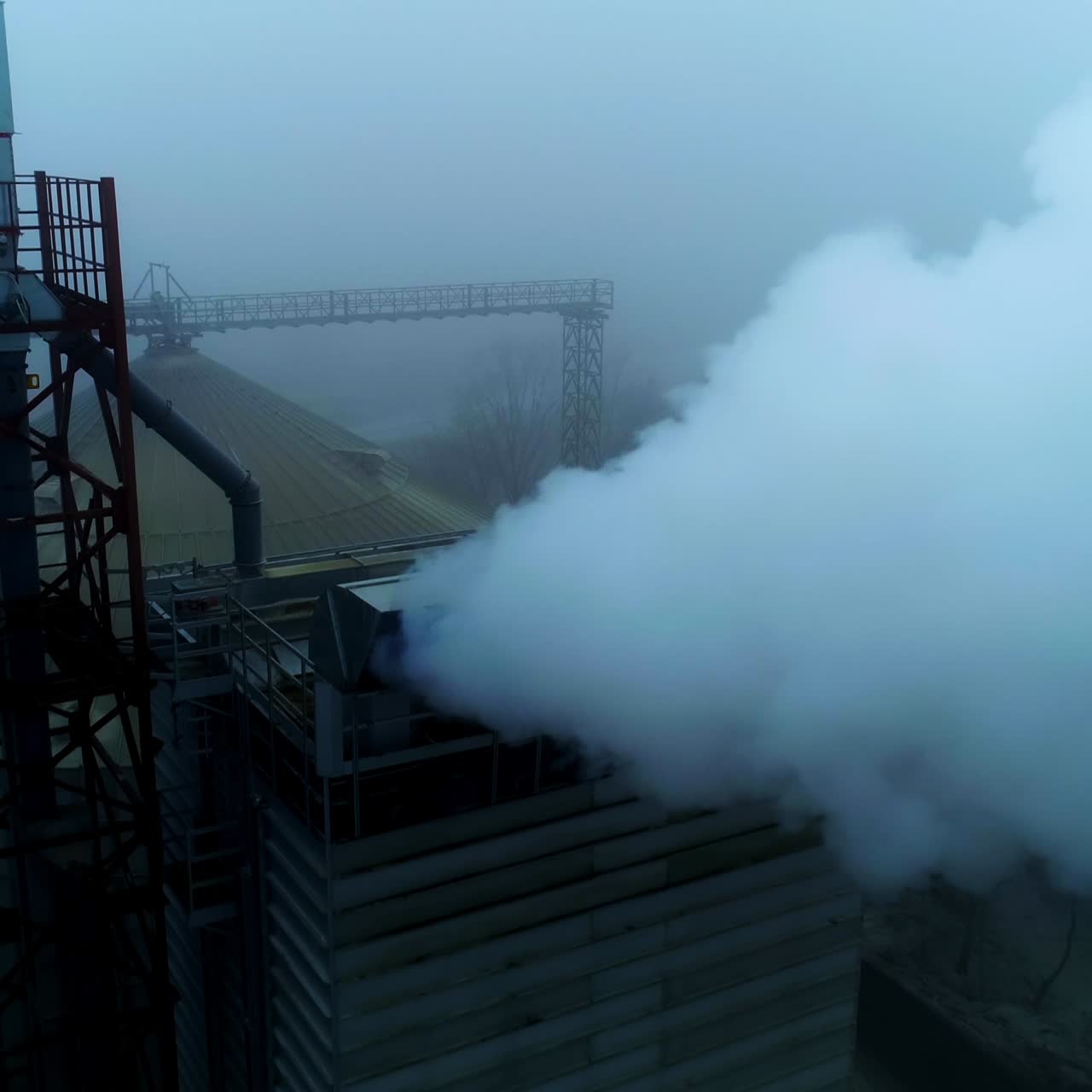 Powerful agribusiness plant for grain storage and processing. Metal tanks and high building with pipes producing thick smoke. Foggy backdrop. Top view