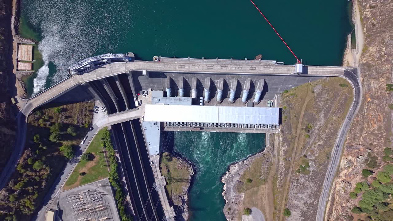 Aerial drone ascends in reverse over Roxburgh Dam, gradually unzooming to showcase the hydroelectric power station, reservoir, and surrounding Central Otago landscape