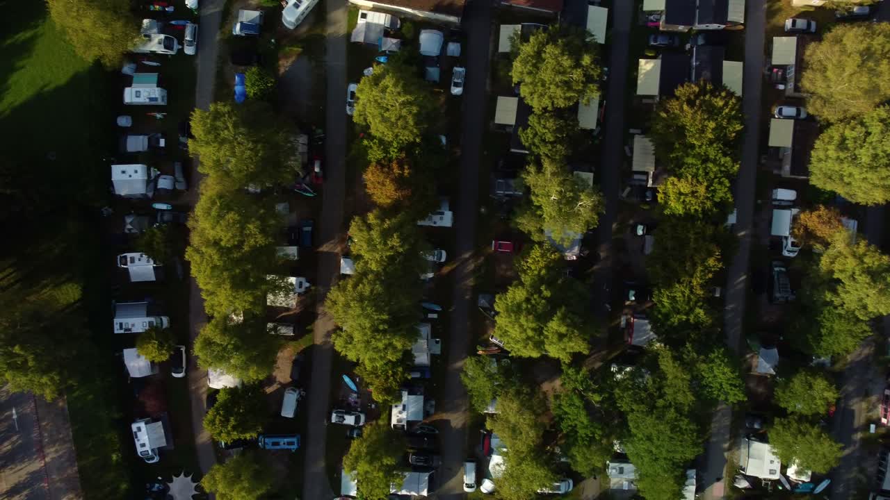 Top down view of a campsite in France. Lac Bleu and the bottom end of Lake Annecy. Drone footages moves to left showing the lines of tents and camper vans separated with paths and lines of trees