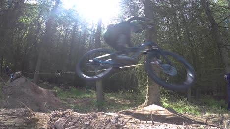 slow motion, group of mountain bikers riding downhill at high speed in forestry track, taking large dirt jump