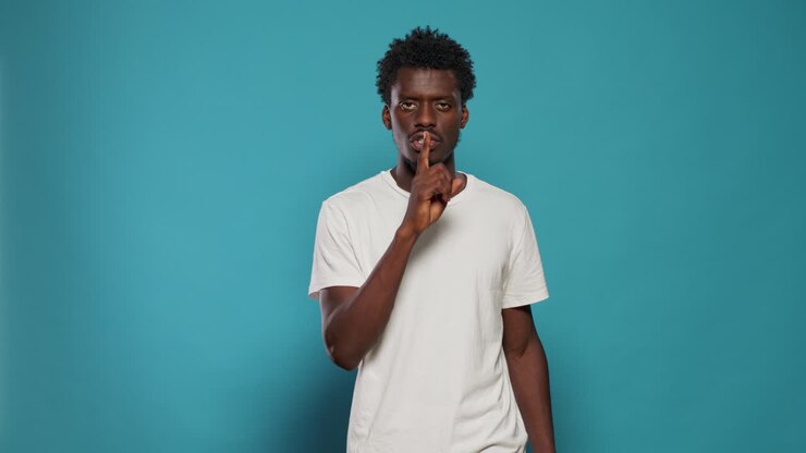 Young man doing silence gesture with finger on mouth