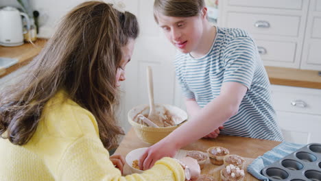 Una-Pareja-Joven-Con-Síndrome-De-Down-Decorando-Pastelitos-Caseros-Con-Malvaviscos-En-La-Cocina-De-Casa