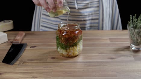 adding oil to ingredients in a glass container to prepare argentinian chimichurri sauce, the perfect sauce for your barbecues