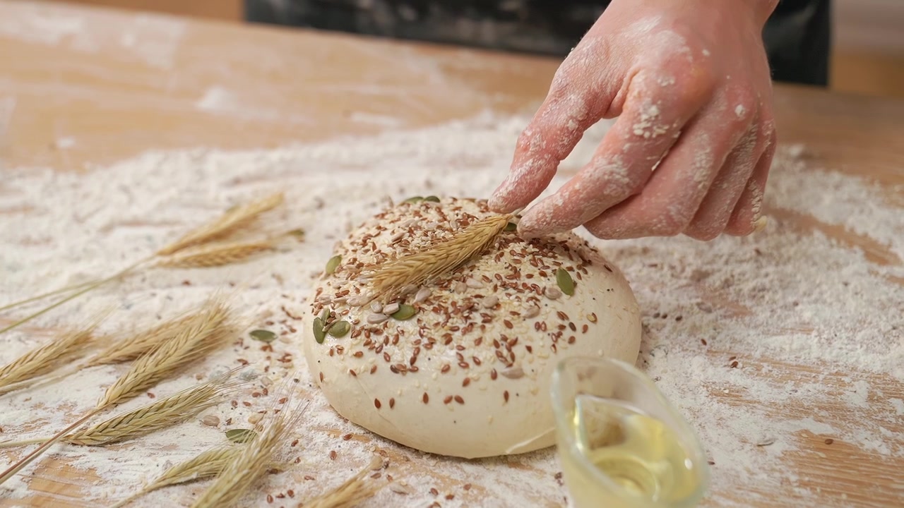 Mão Decorando Massa de Pão Fresca com Sementes e Trigo