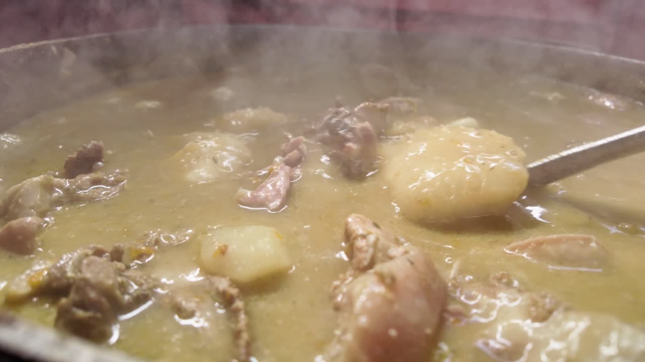 Detailed shot of a steaming pot of Dominican Sancocho, with a metal spoon stirring boiling meats and vegetables, showcasing the steam and rich ingredients of this traditional dish.