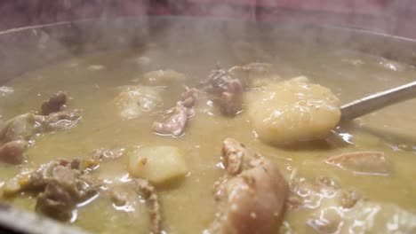 detailed shot of a steaming pot of dominican sancocho, with a metal spoon stirring boiling meats and vegetables, showcasing the steam and rich ingredients of this traditional dish.