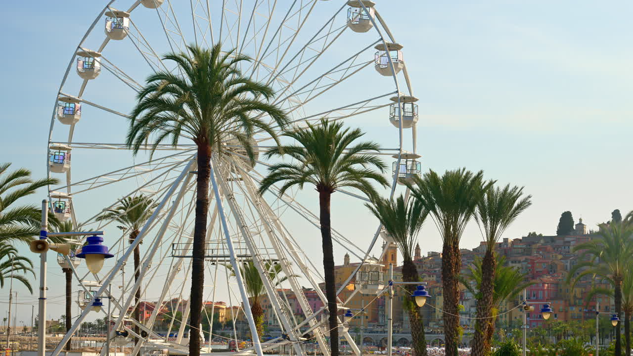 View of a white Ferris Wheel on the beach in Menton, France with the city on the background