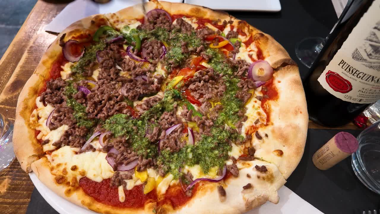 Ripresa dall'alto di olio d'oliva versato a filo su una pizza gourmet con carne di manzo e salsa al pesto