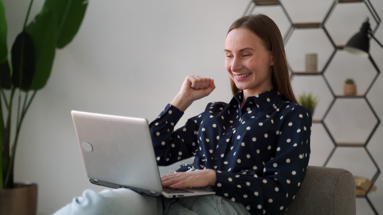 집에서 소파에 앉아 노트북으로 일하면서 무언가를 축하하는 예쁜 여자.