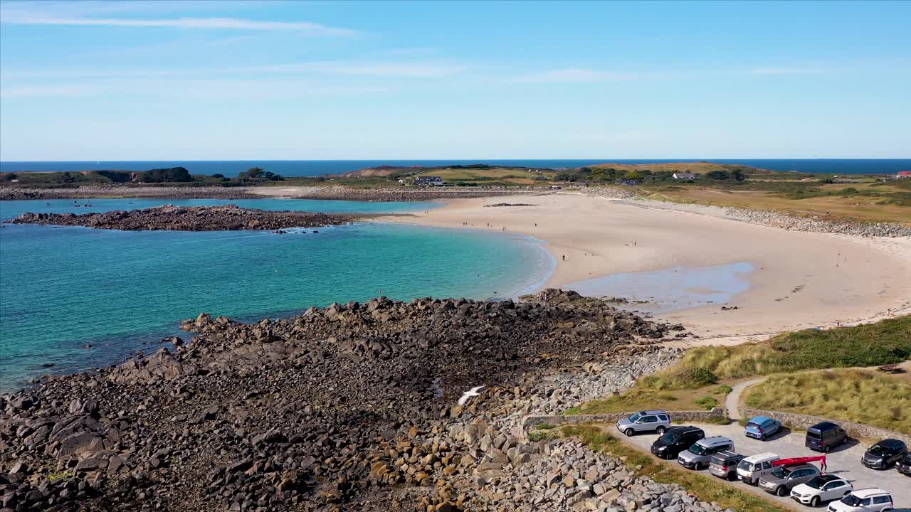 Drone footage over north Guernsey coastline with summer beach activities and successive sandy bays on sunny day with birds flying past