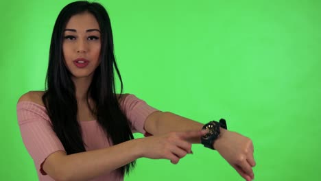 young attractive asian woman points to watch - green screen studio