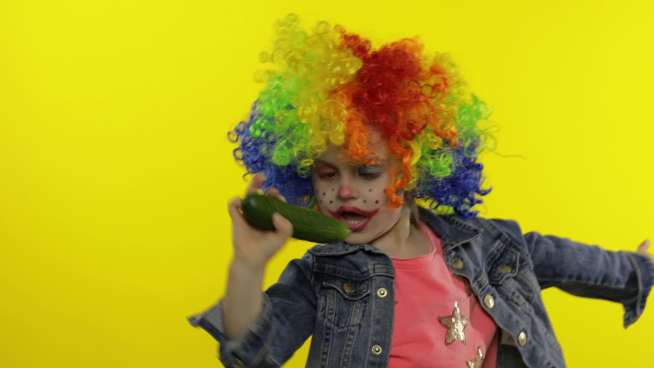 una niña payasa con una peluca arco iris haciendo caras tontas, cantando, sonriendo, bailando. halloween