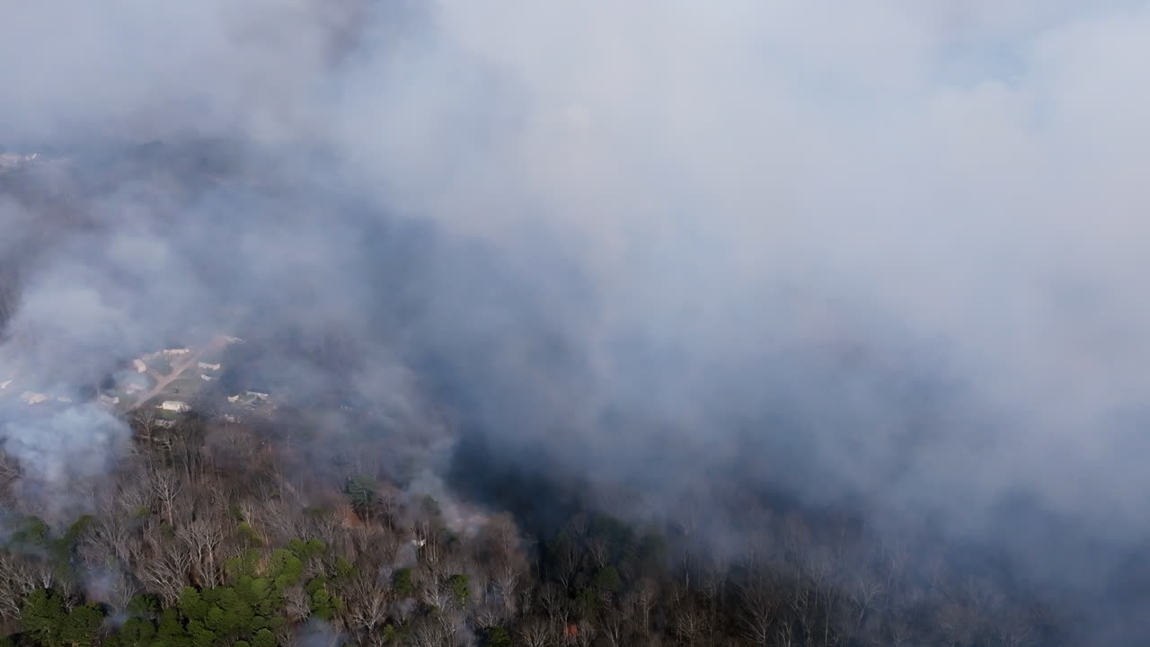 Aerial footage of a neighborhood and forest that is covered in smoke from a forest fire.