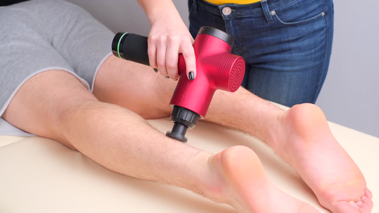 masajista femenina masajeando los músculos de la pantorrilla de un deportista con un masajeador de percusión