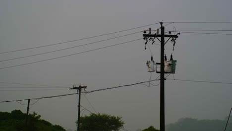 Silueta-De-Postes-Y-Cables-Eléctricos-Contra-Un-Cielo-Brumoso,-Insinuando-Infraestructura