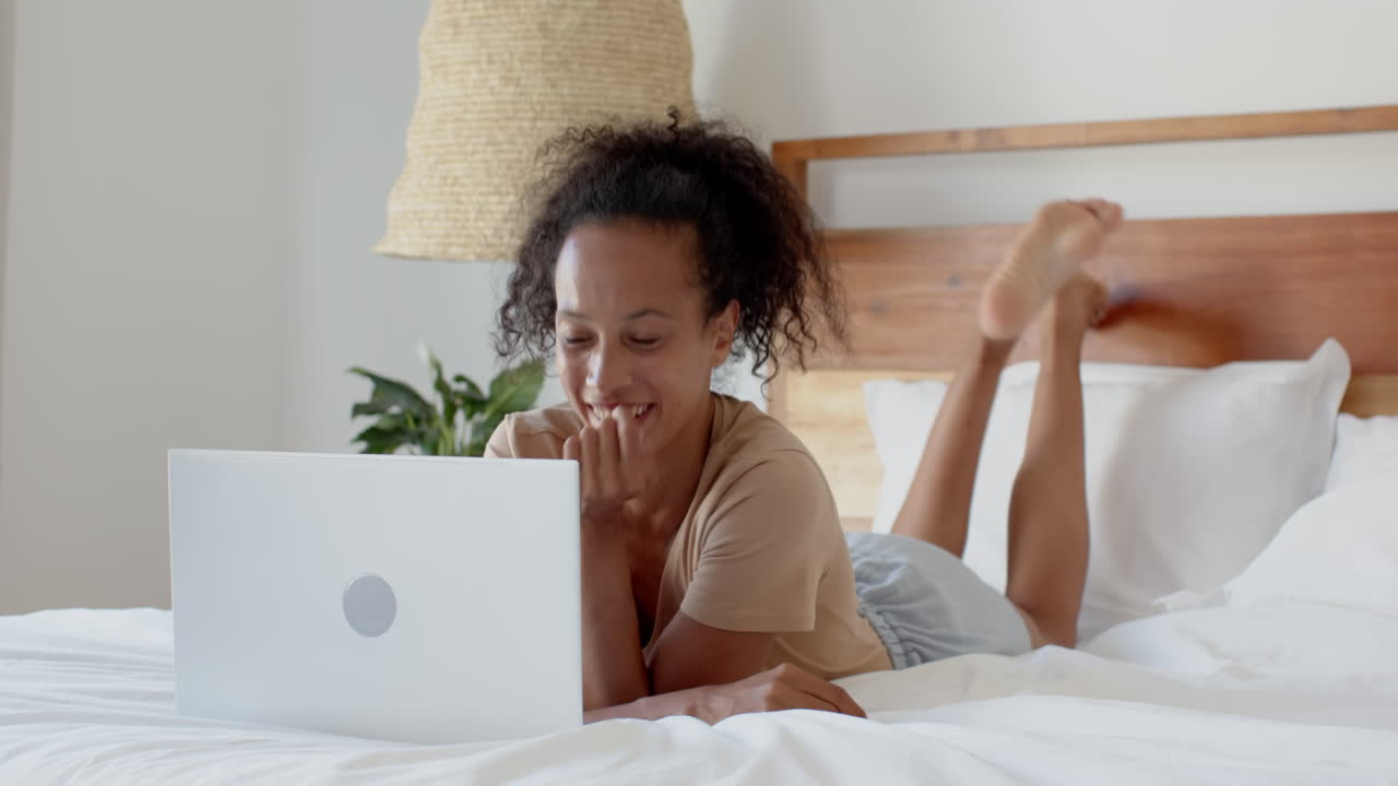 Young woman relaxing on bed using laptop, focused on work from home