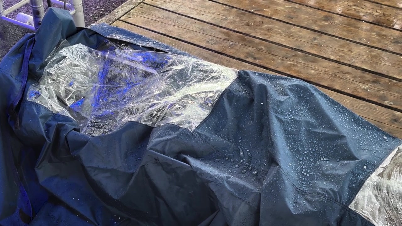 Close-up of a waterproof protective tarp covering outdoor furniture during hailstorm, showing raindrops and weather protection concept on a wooden terrace.