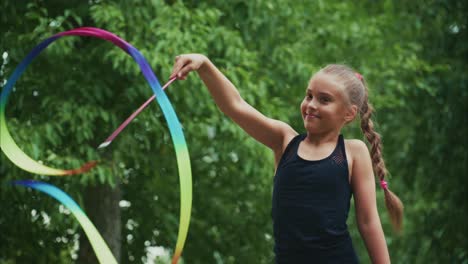 a young girl dances gracefully with colorful ribbons in a lush green park, showcasing her skills in rhythmic movement and creativity under natural light