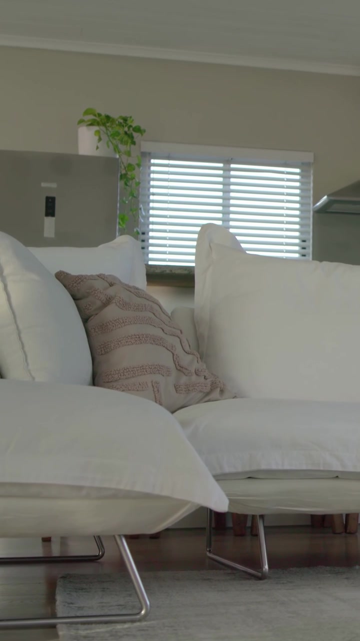 Vertical video: Tilting camera revealing white sectional sofa in living room to show kitchen layout