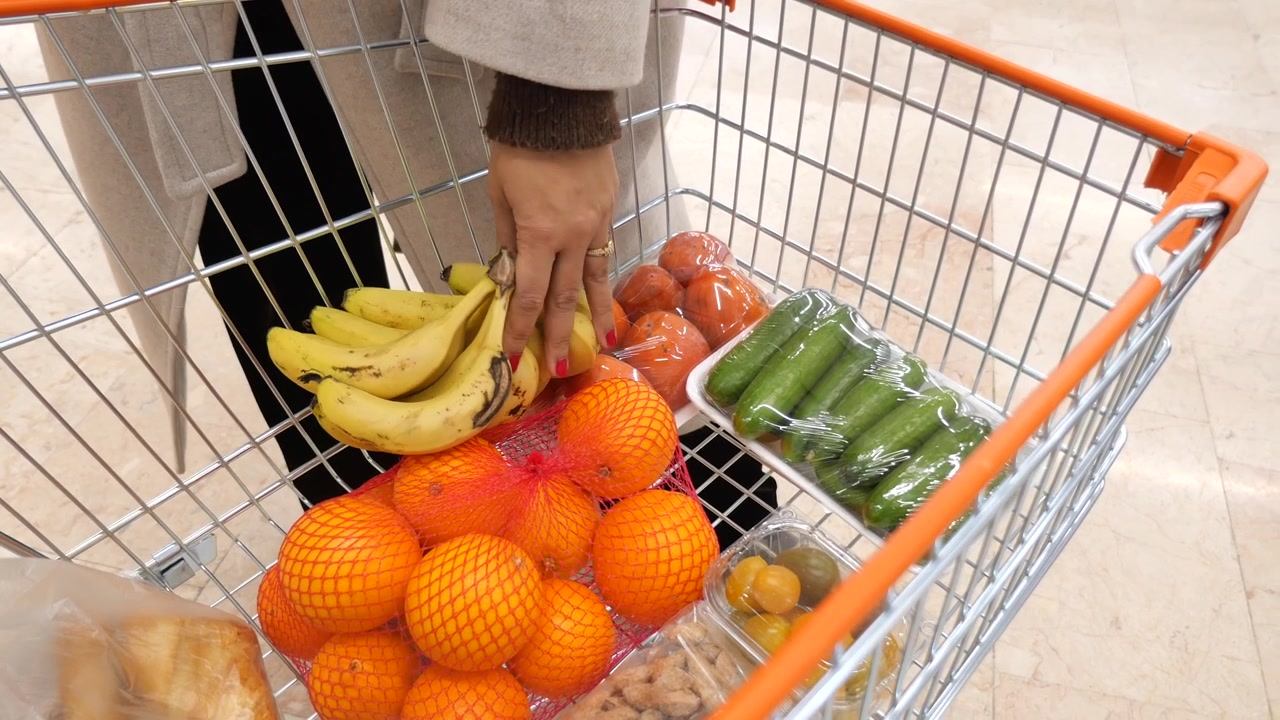 Persona che mette banane in un carrello della spesa pieno di generi alimentari