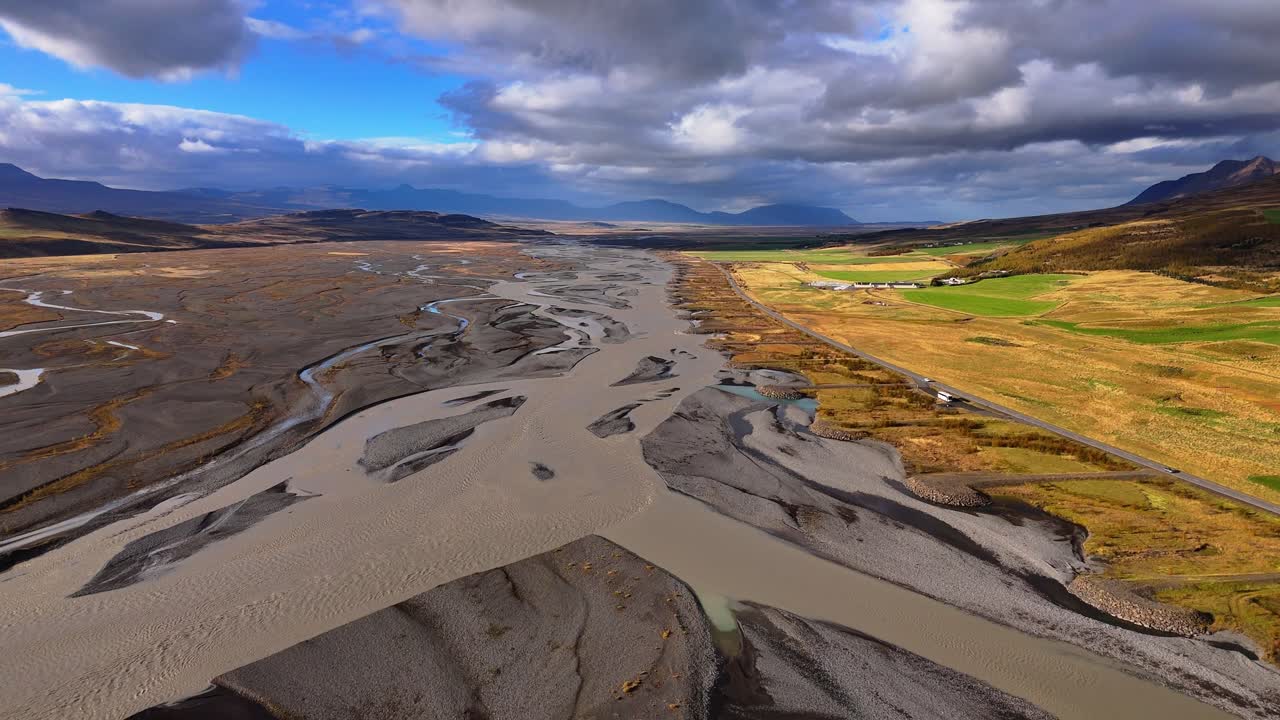 Icelandic streams of glacial wash twist like veins on their journey through glaciated valleys, volcanic rock and vibrant mossy green flatlands to sea. Drone aerial, blue sky clouds on the horizon