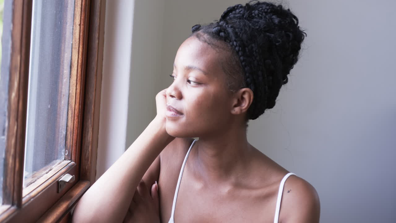 Young African American woman gazes out a window, with copy space