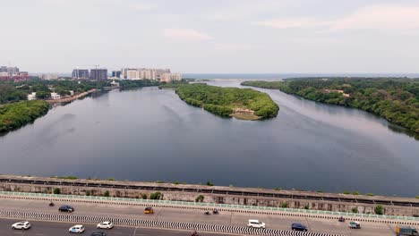 aerial side view of vehicles apssing over bridge with small green lush island at background.