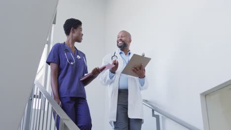 Médicos-Afroamericanos,-Hombres-Y-Mujeres,-Sosteniendo-El-Portapapeles-Y-Hablando-En-El-Hospital