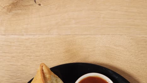 Top-shot track-in close-up of a plate of Samosa served with condiments