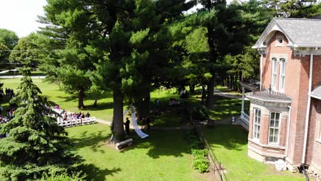 aerial drone shot that begins on an old historical brick home and ends on a beautiful outdoor wedding with the seats starting to fill up.  this wedding is located in nevada, iowa.