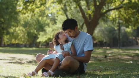 Happy-little-Asian-girl-eating-chocolate-ice-cream-with-her-father-and-kissing-him-in-park