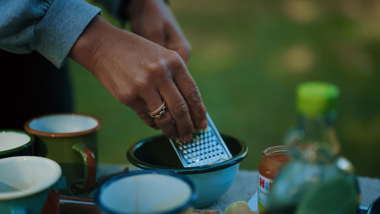 Close-up of a hand grating fresh ginger into a bowl outdoors with soft nature in the background