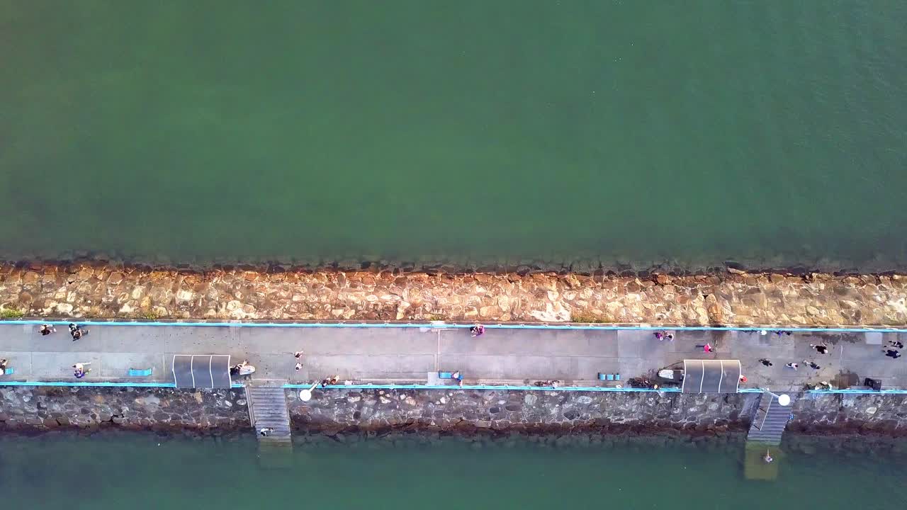 민간인을 위한 포장된 통로가 있는 돌로 만든 방파제 부두의 역동적인 하향식 공중 촬영