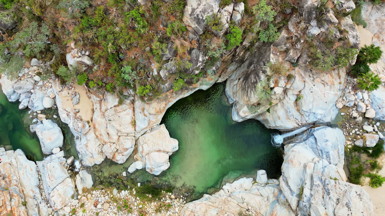 Aerial drone view of a canyon with a small waterfall falling into a natural pool surrounded by rocky cliffs in Baja California, Mexico