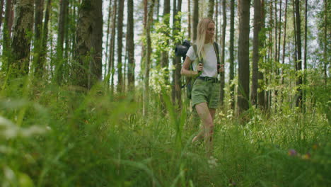 A-woman-walks-through-the-woods-on-a-sunny-summer-day-in-shorts-and-a-T-shirt-smiling-and-examining-the-beauty-of-nature-and-the-forest