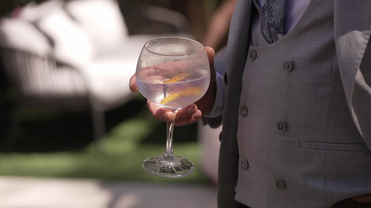 Uomo in abito formale che tiene un grande bicchiere di cocktail all'aperto