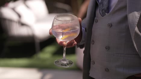 man in formal attire holding a large glass of cocktail outdoors